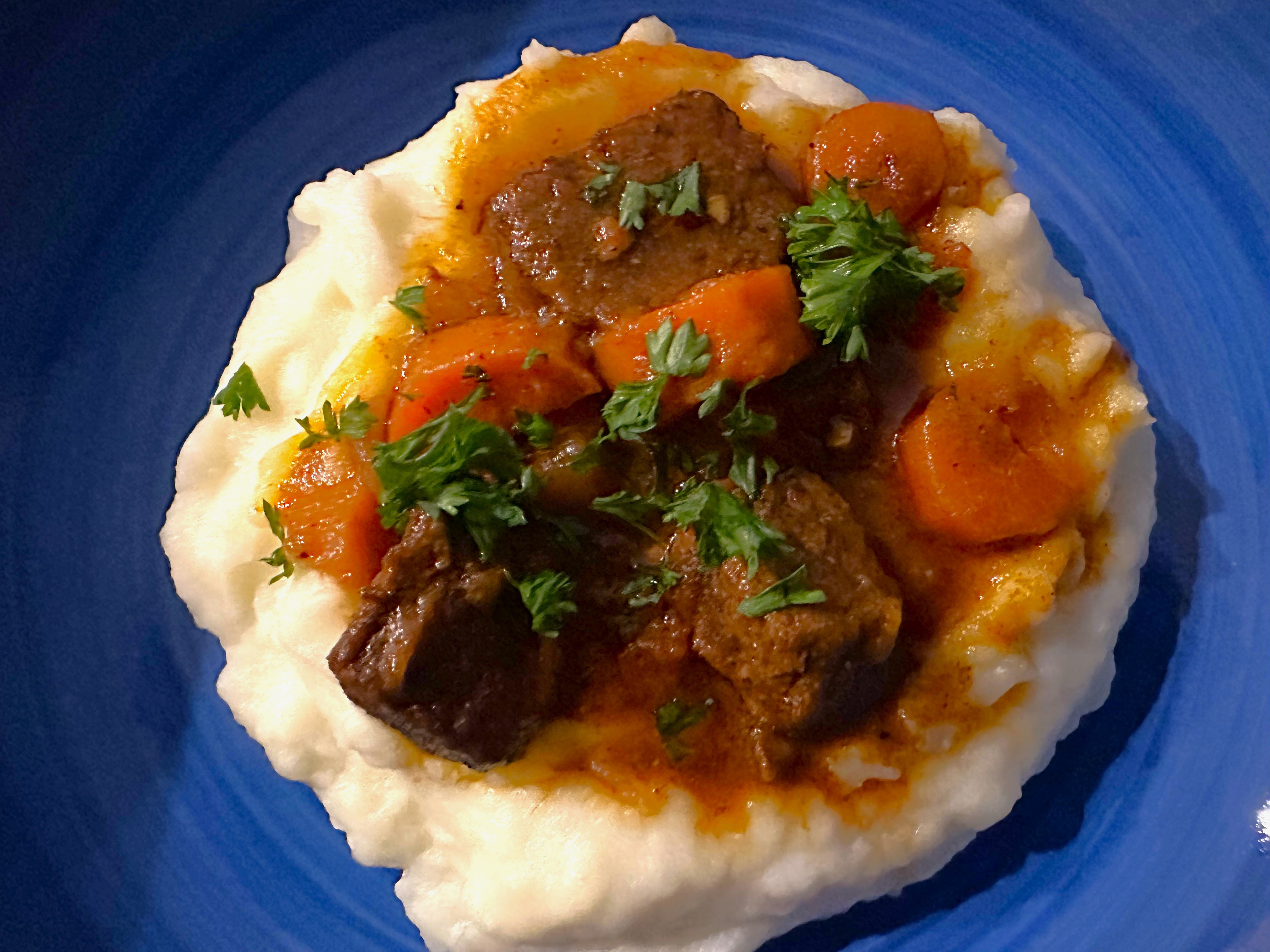 Ancho Chile Beef Stew on top of mashed potatoes in a blue bowl.