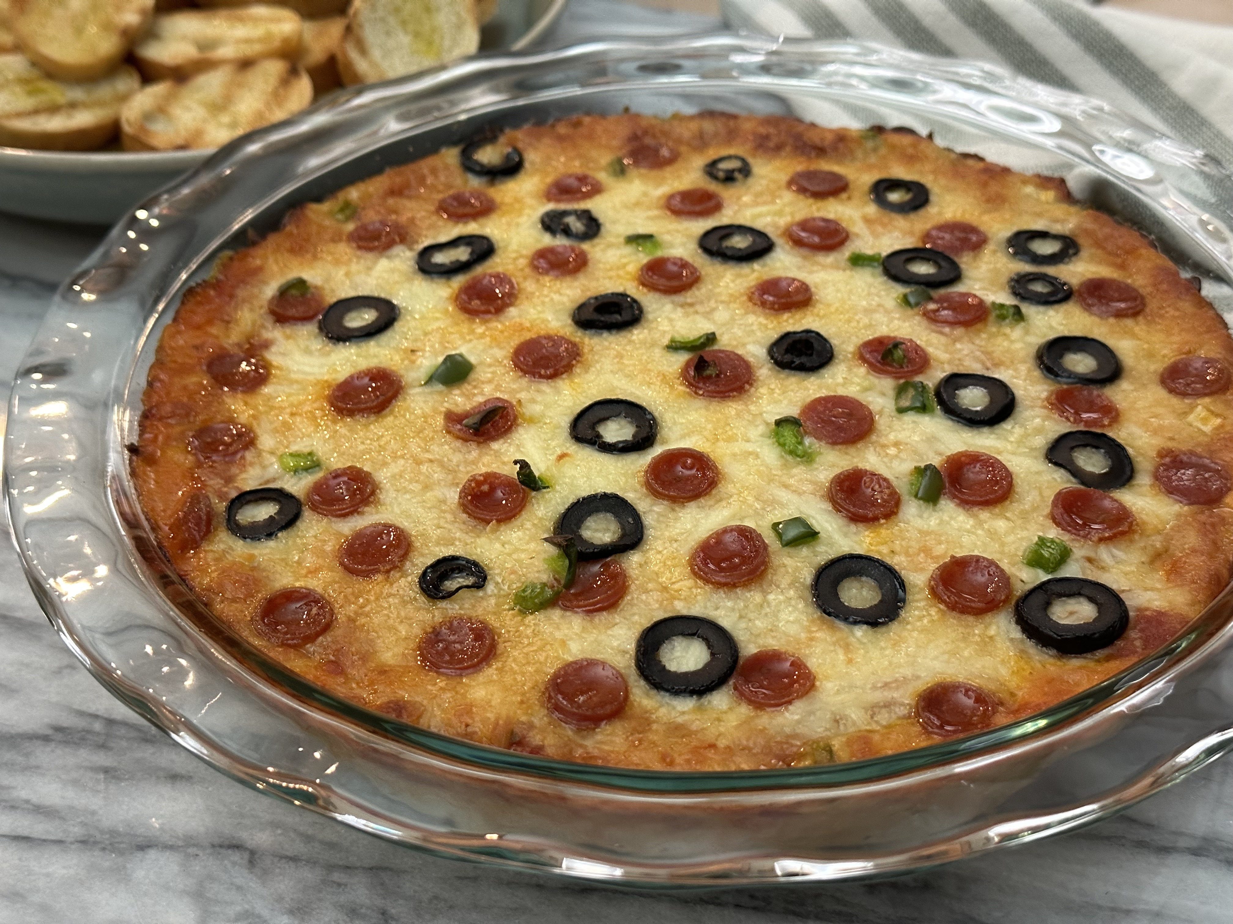 Hot Pizza Dip in a clear glass pan with toasted bread on a plate.