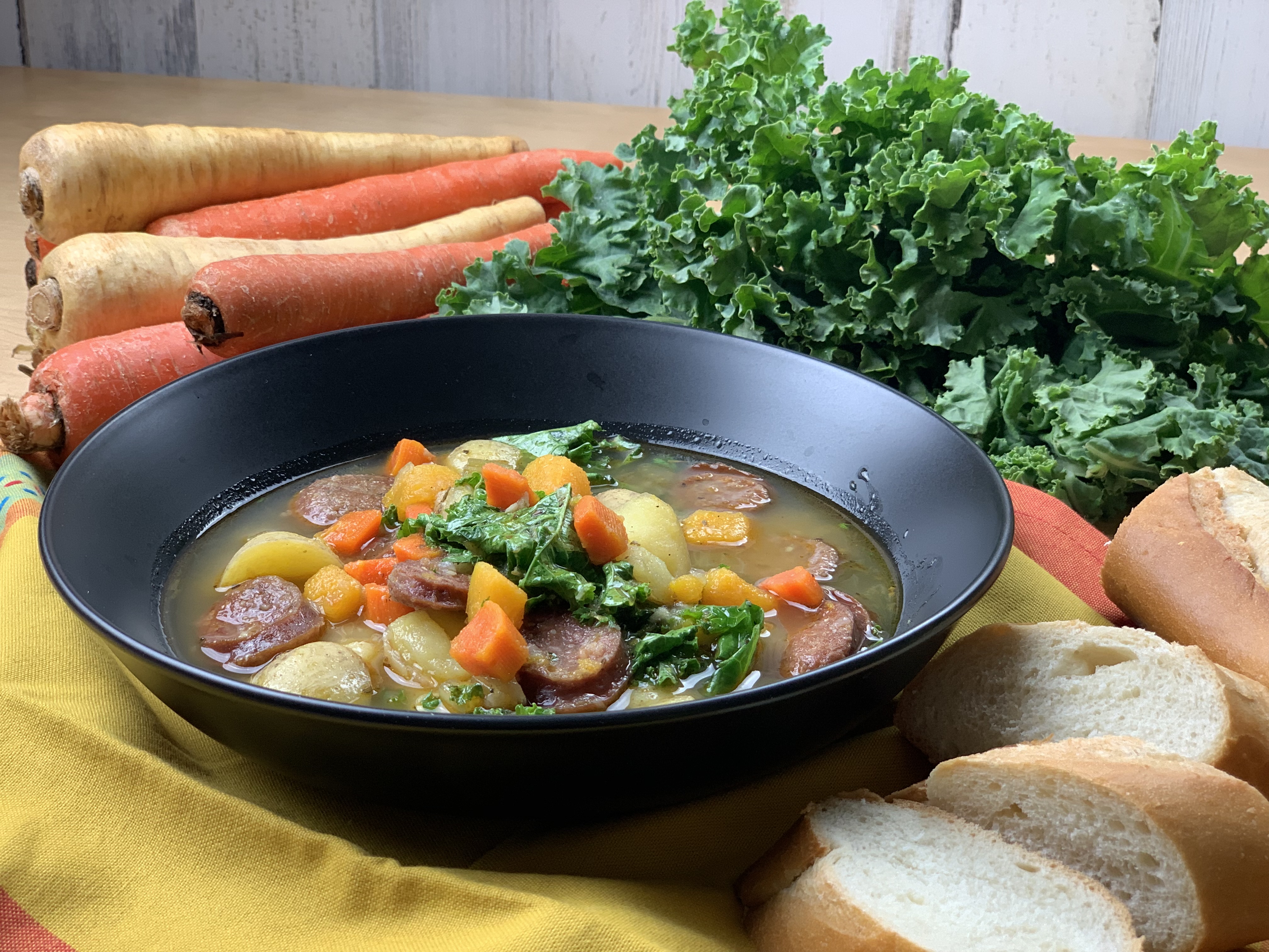 Bowl of Sausage, Sweet Potato and Kale Soup with fall vegetables in the background.