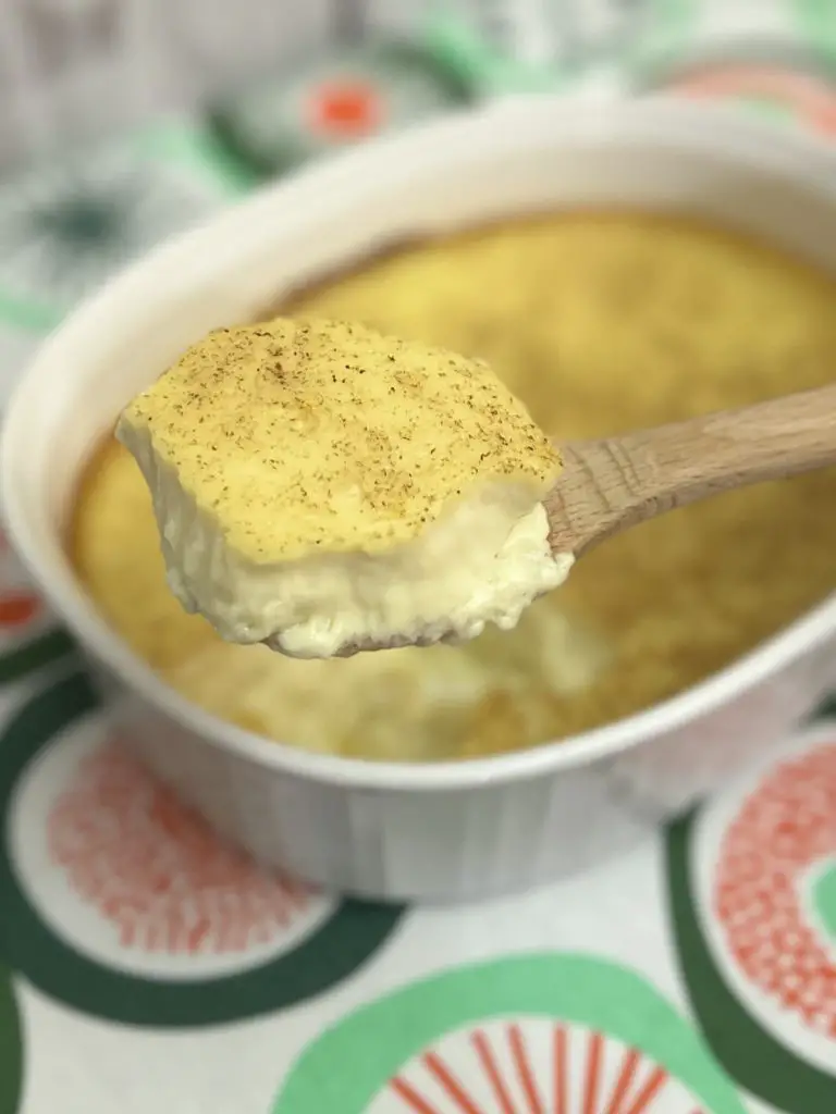 Baked Custard scoop on a wooden spoon with pan in the background.