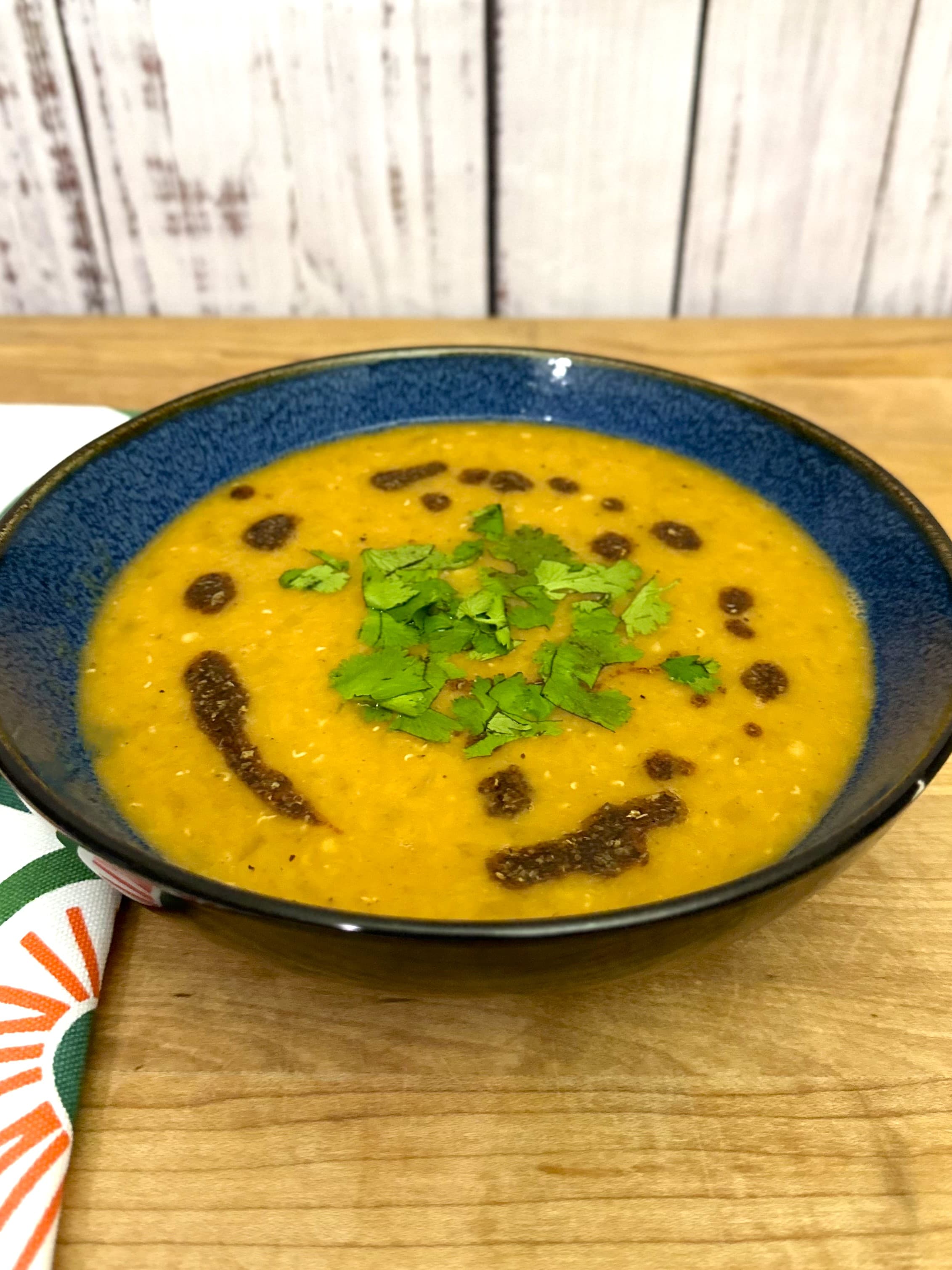 Red Lentil Soup in a blue bowl on a wooden board.