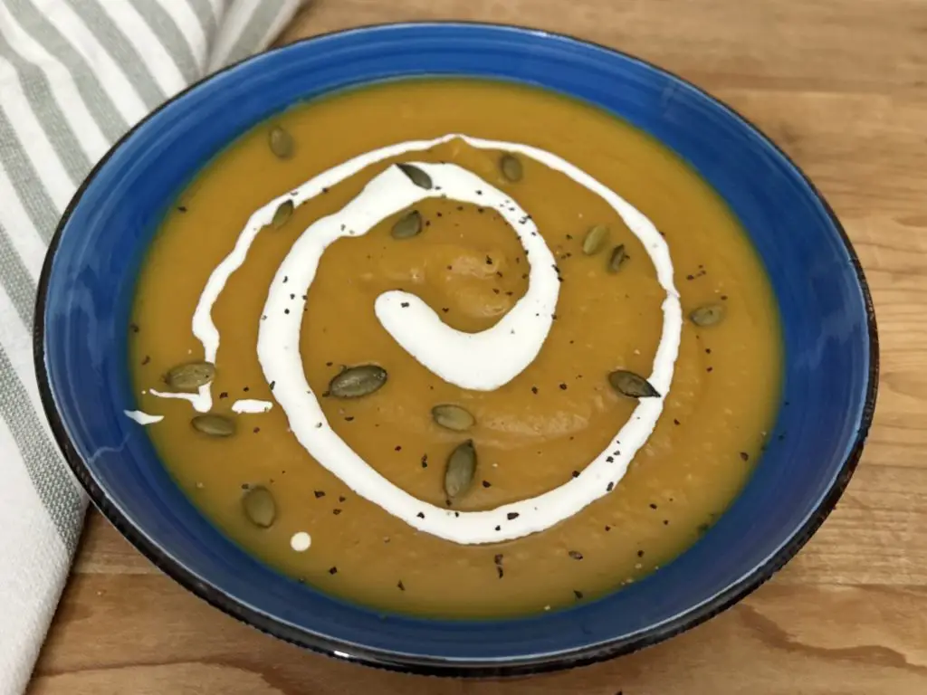 Roasted Butternut Squash Soup in a blue bowl on a wooden board with a striped napkin.