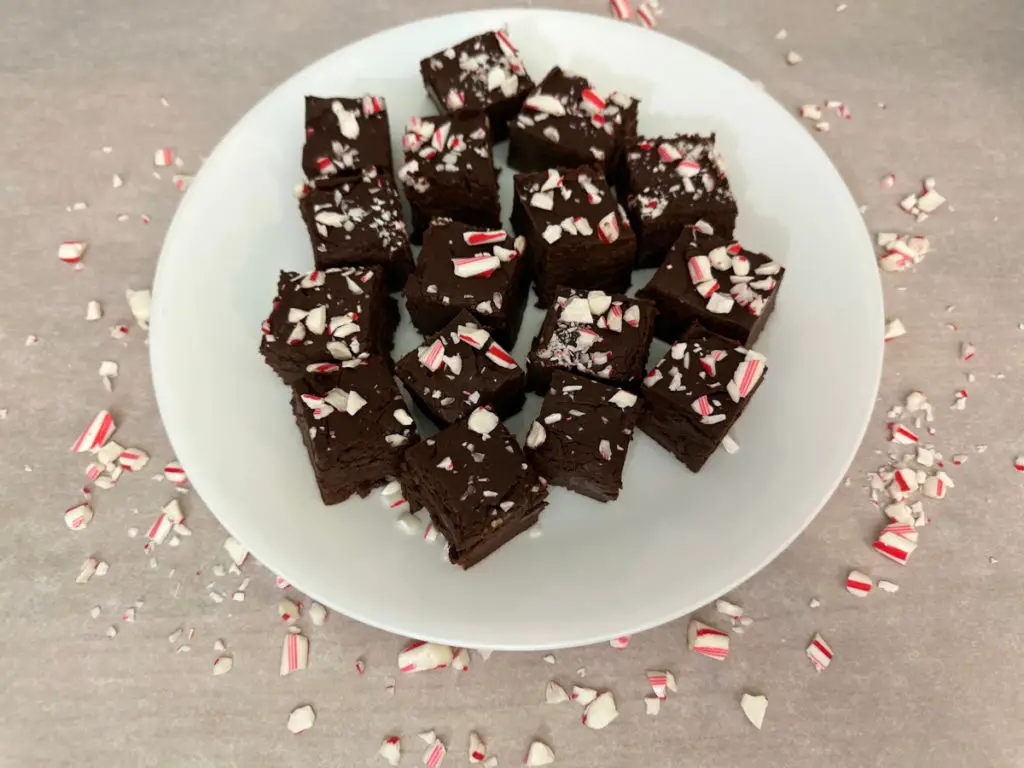 Peppermint Fudge on a white plate with bits of peppermint on parchment paper.