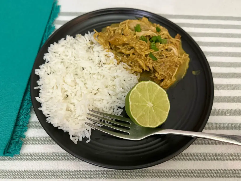 Chicken Tikka Masala with white rice and lime on a black plate.