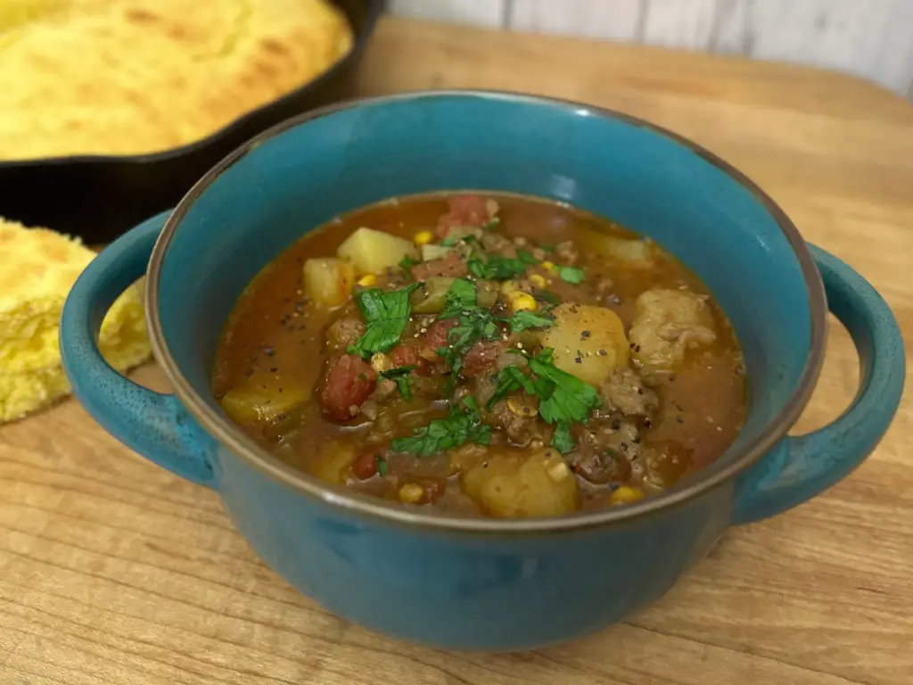 Cowboy stew in a blue bowl, with skillet cornbread on the side.