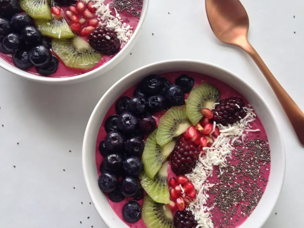 Two Acai Berry Smoothie bowls with a copper spoon.