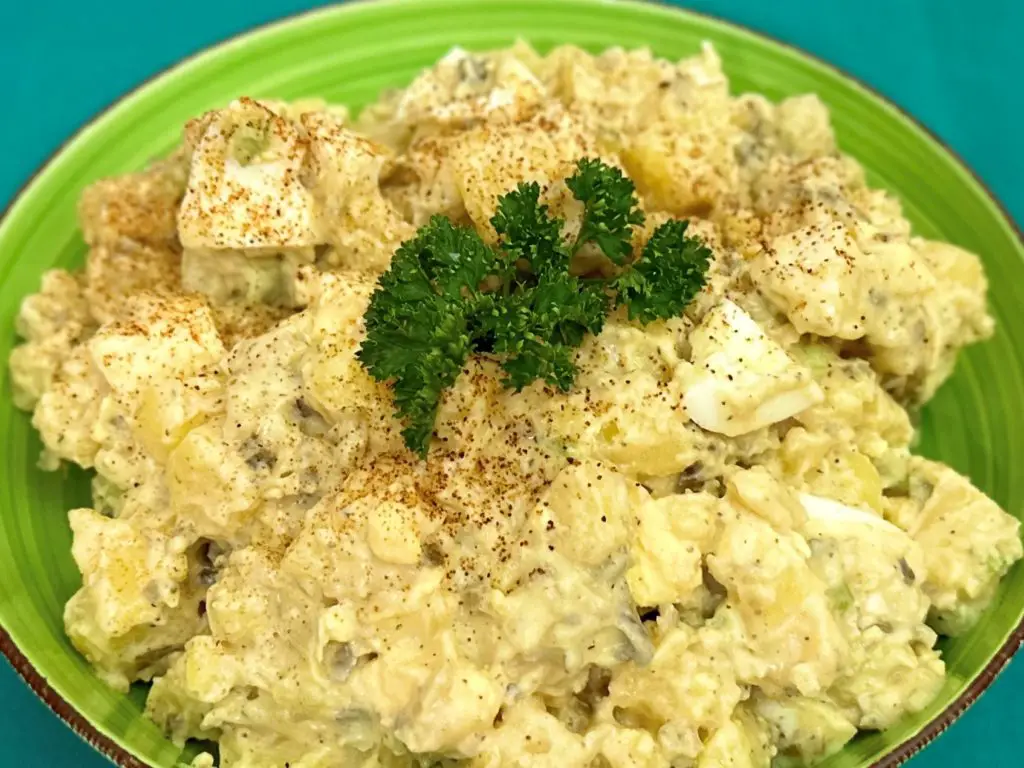 Spicy cajun potato salad in a green bowl on a blue background.